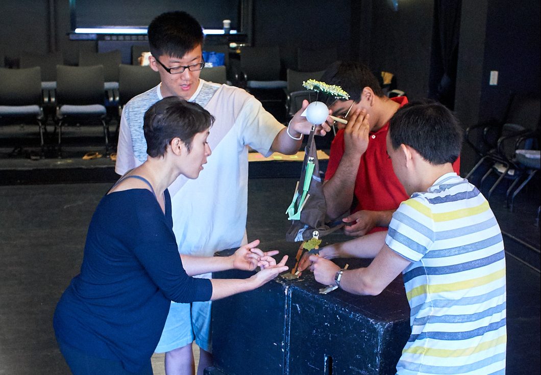 Three students animating a puppet, guided by teacher